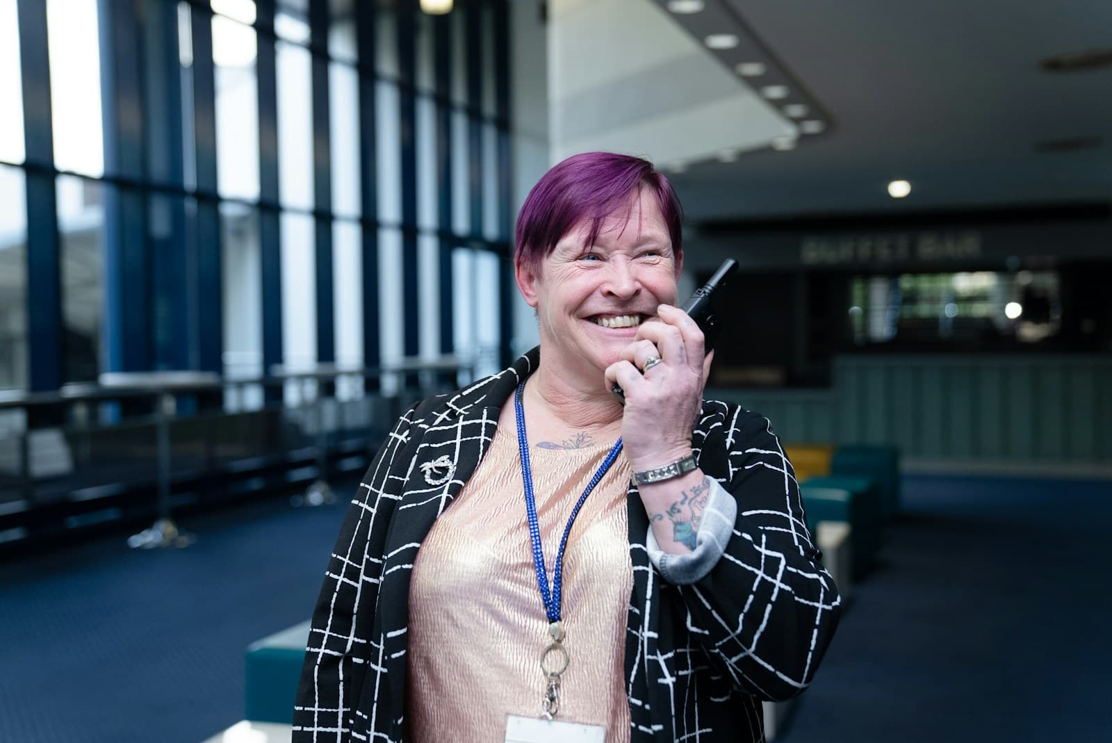 A smiling event coordinator wearing a lanyard and talking into a two-way radio
